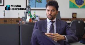 Fábio Faria sentado em um sofá preto e gesticulando.